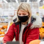 Młoda kobieta w czarnej masce medycznej w supermarkecie w dziale z owocami i warzywami.