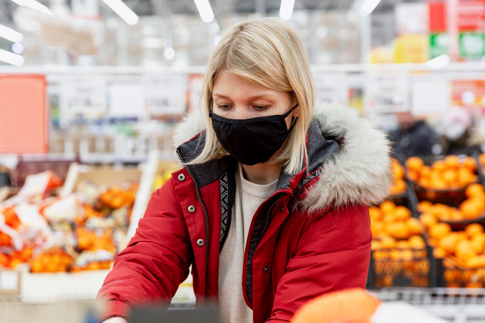 Młoda kobieta w czarnej masce medycznej w supermarkecie w dziale z owocami i warzywami.