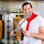 Doner kebab - przyjazny sprzedawca w tureckiej knajpce fast food, krojenie mięsa ostrym nożem przed szpikulcem