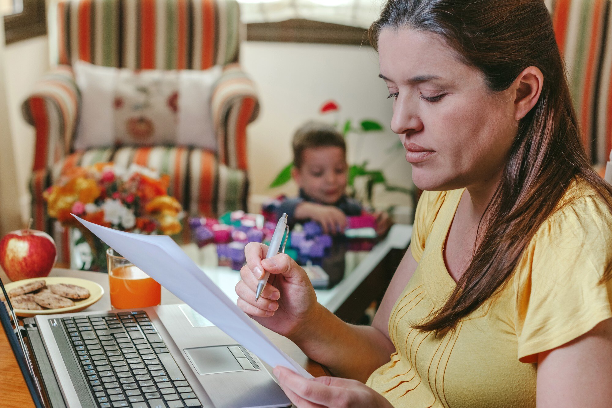 Matka pracuje na laptopie w salonie, podczas gdy jej syn się bawi