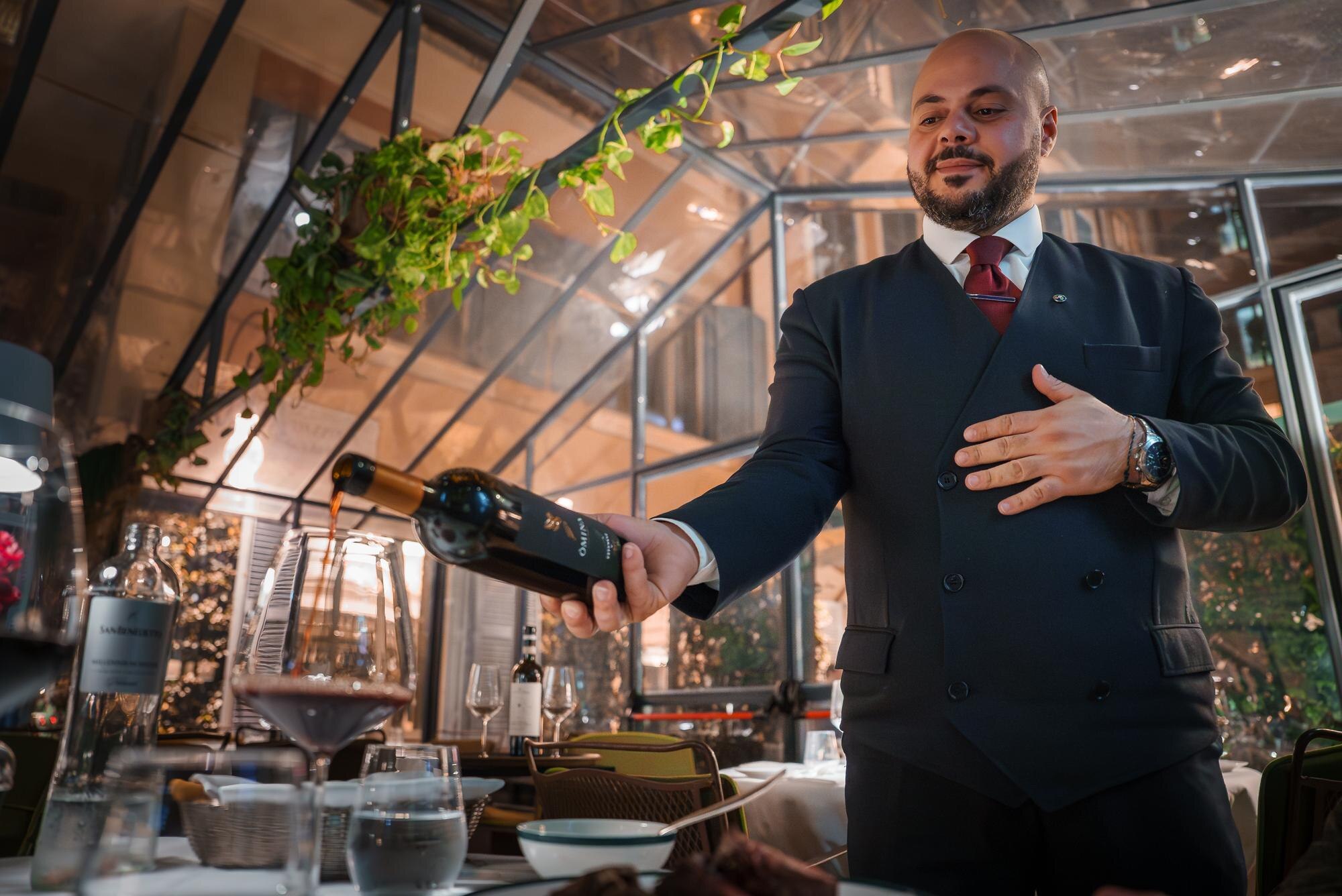 Pewny siebie kelner prezentujący wino w luksusowej restauracji