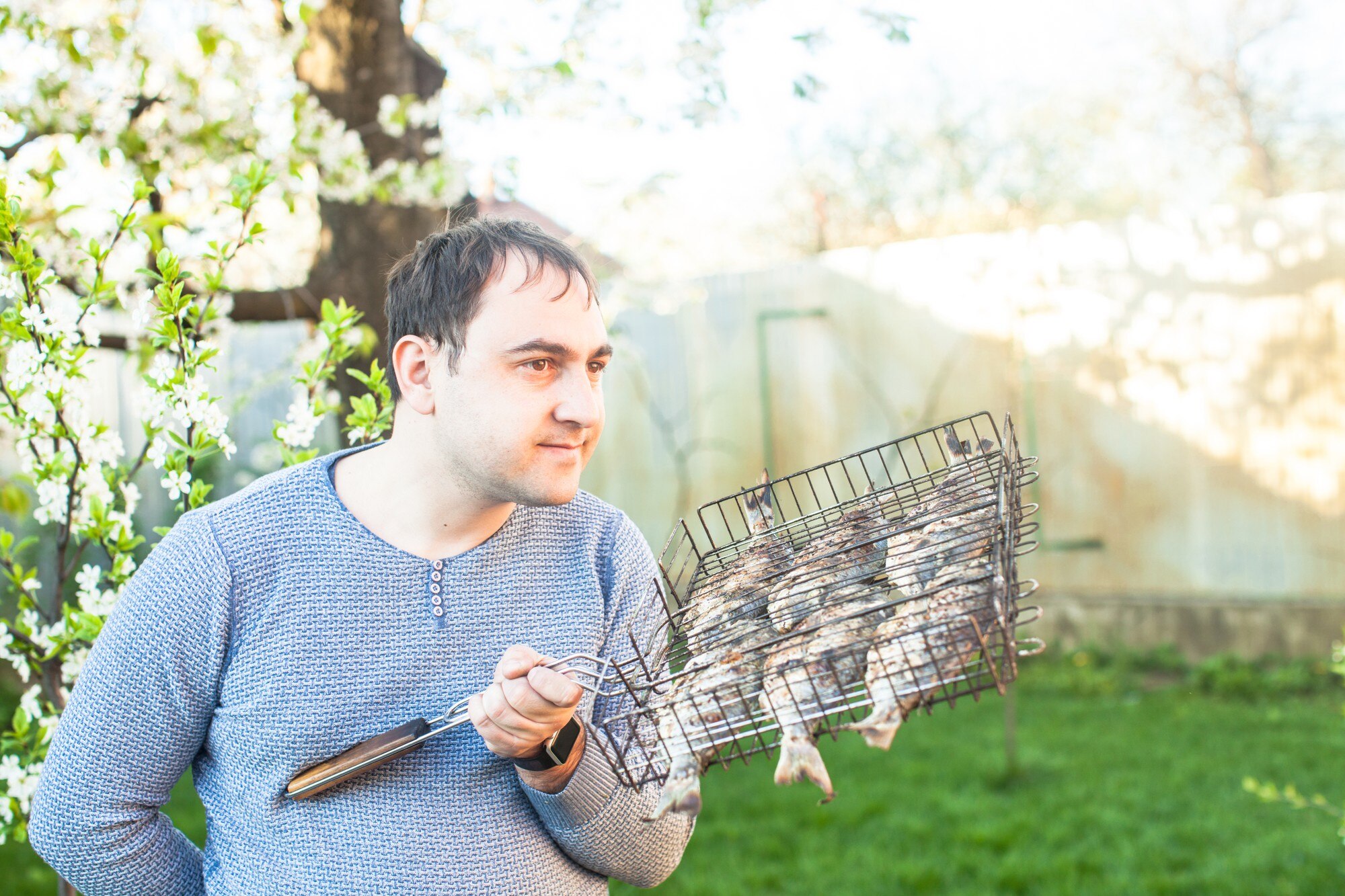 Mężczyzna trzymający grillowaną rybę w stalowej siatce
