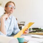 zdziwiona młoda kobieta architekt w okularach pracująca z rysunkami podczas projektowania szkicu w miejscu pracy