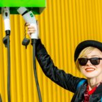Szczęśliwa kobieta ładuje samochód elektryczny na stacji ładującej