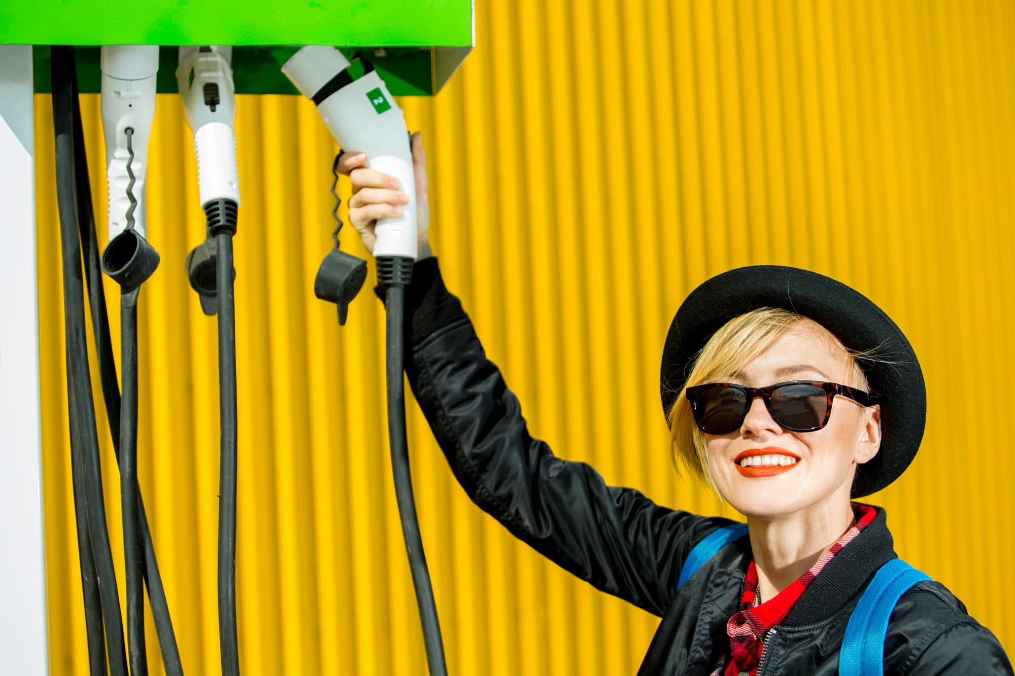 Szczęśliwa kobieta ładuje samochód elektryczny na stacji ładującej