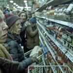 Grupa ludzi biegnących przez sklep spożywczy z wózkami na zakupy