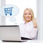 biznes, ludzie, sprzedaż, gesty i koncepcja technologii - uśmiechnięta kobieta lub studentka pokazująca kciuk w górę z laptopem i wózkiem na zakupy w dymku tekstowym w biurze