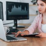Korzystając z laptopa Kobieta makler giełdowy w zwykłych ubraniach pracuje w biurze za pomocą komputera