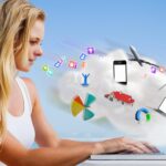 Ładna blondynka używa swojego laptopa na plaży przeciwko grafice przetwarzania w chmurze z aplikacjami