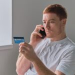 Mężczyzna płaci kartą kredytową na smartfonie w domu Sklep z płatnościami online na telefonie komórkowym Mężczyzna trzyma kartę kredytową i używa smartfona do zakupów online