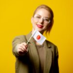 Stylowa blondynki kobieta w kurtce z japończyk flaga na kolorze żółtym
